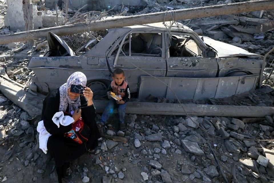 / Una mujer palestina y un niño descansan entre los escombros junto a un automóvil destruido mientras la gente inspecciona los daños a sus hogares a su regreso al distrito de Khezaa,