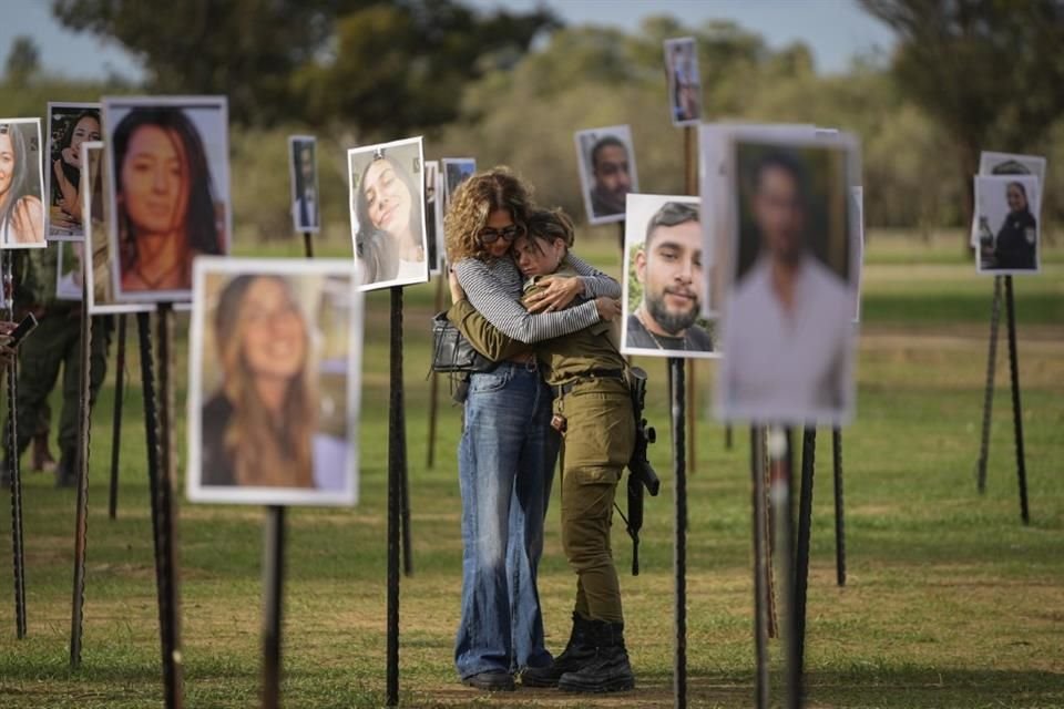 Dos mujeres israelíes se abrazan rodeadas de fotos de personas asesinadas o secuestradas por Hamas durante un ataque el 7 de octubre.