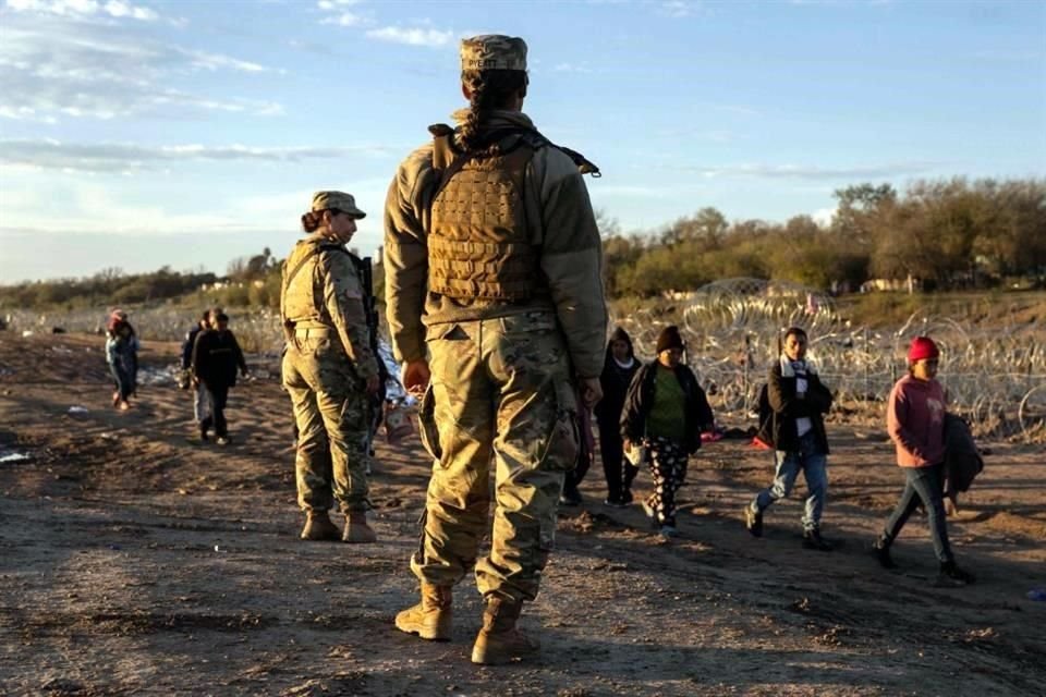 Soldados de la Guardia Nacional de Texas observan mientras miles de inmigrantes caminan hacia un centro de tránsito de la Patrulla Fronteriza de EU.