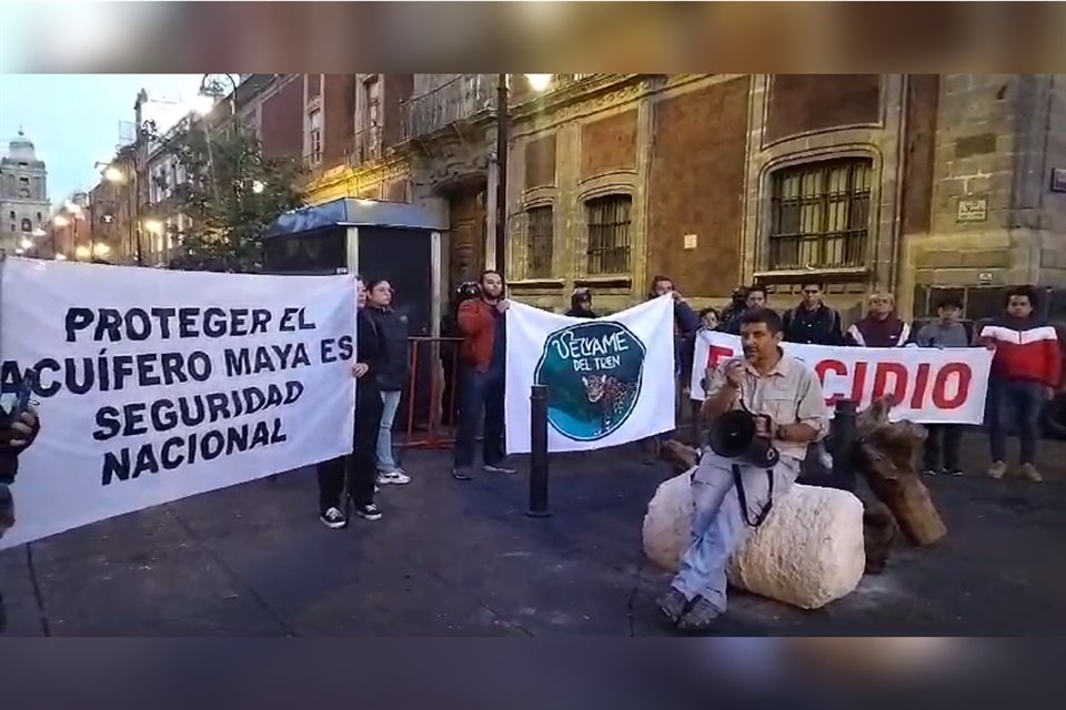 Con piedra caliza y la raíz de un árbol talado por el Tren Maya, integrantes de #SélvameDelTren se manifestaron afuera de Palacio Nacional.