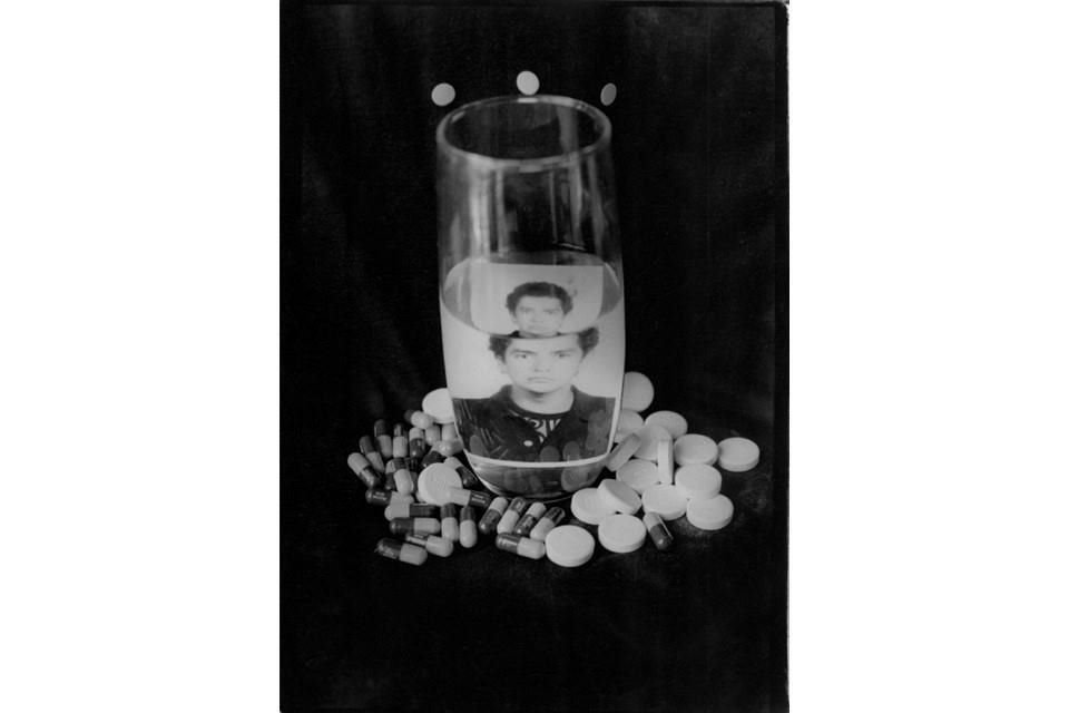 Del portafolio Adherencia es 'Ajustada cárcel que me cubre (1997)', una composición donde un retrato de Óscar Sánchez, magnificado y encerrado en un vaso de agua, se encuentra rodeado de pastillas.