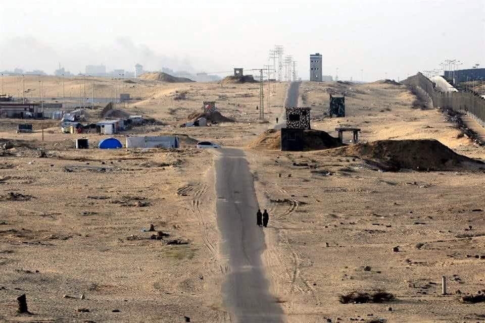 Dos mujeres caminan por una carretera asfaltada en medio de un campamento desierto para palestinos desplazados en la frontera con Egipto en Rafah.