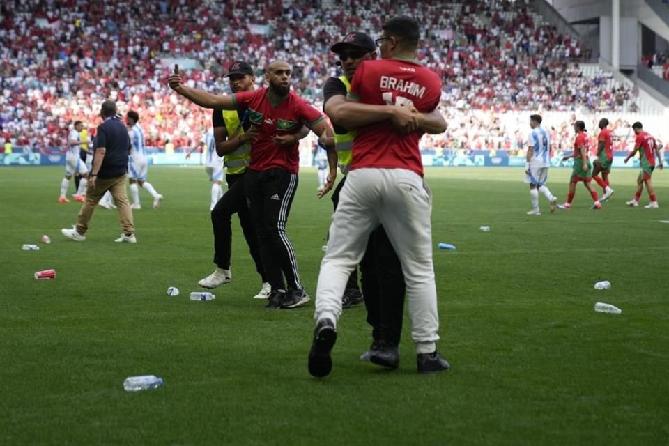 Los elementos de seguridad detienen a los aficionados que saltaron a la cancha.