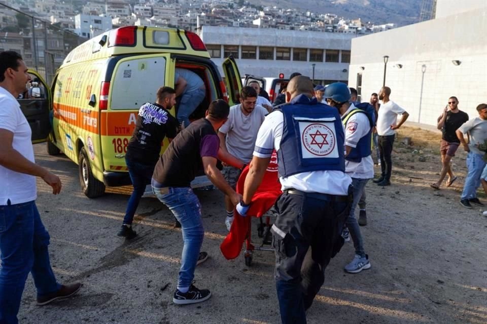 Las fuerzas de seguridad y los médicos israelíes transportan a las víctimas junto con los residentes locales, en un lugar donde se informó que cayó un ataque desde el Líbano.