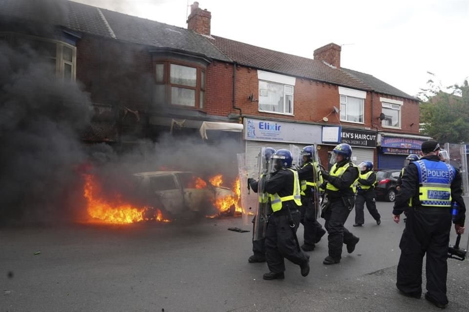 Un auto en llamas durante una protesta anti migración en Inglaterra.