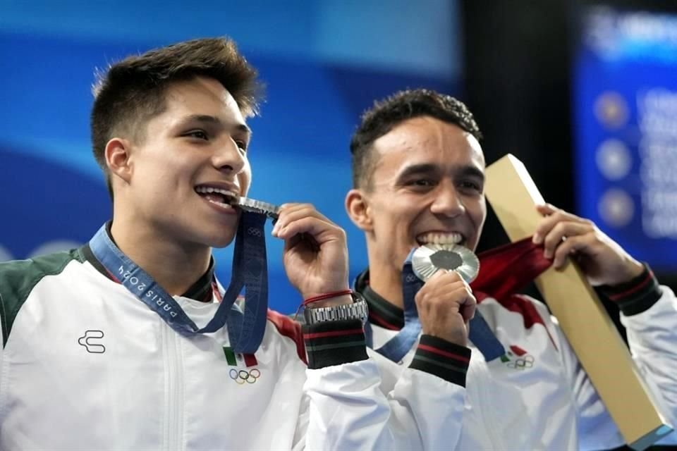 Los mexicanos Juan Manuel Celaya Hernández y Osmar Olvera Ibarra muerden su medalla de plata en el podio después de la final de saltos sincronizados de trampolín de 3 metros en los JO de París 2024.