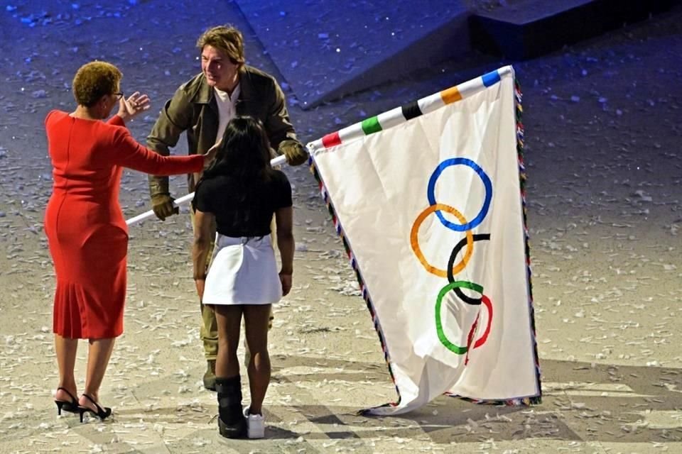 Tom Cruise recibe la bandera olímpica de manos de la alcaldesa de Los Ángeles, Karen Bass, y de la gimnasta estadounidense Simone Biles.