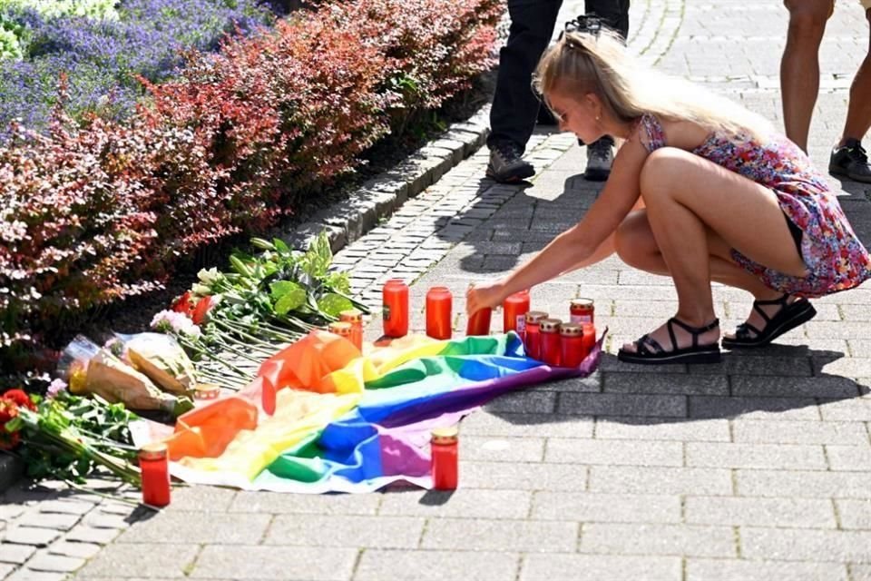 Una joven enciende una vela en un monumento improvisado con flores y una bandera arcoíris en memoria de las víctimas.