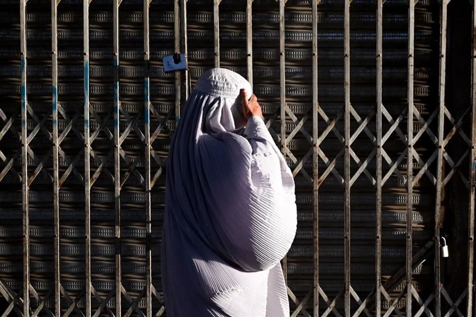 Una mujer camina junto a una tienda cerrada en Kandahar.