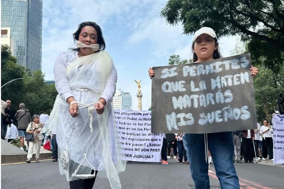 Una mujer vestida de la justicia posa junto a un letrero que dice 'si permites que la maten, matarás mis sueños'.