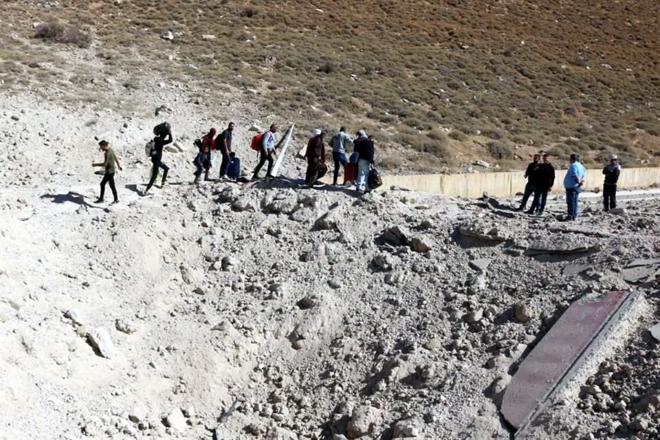 Personas que huyen de los bombardeos israelíes en el Líbano, caminan alrededor de un cráter causado por un ataque israelí, en la zona de Masnaa, en el lado libanés del cruce fronterizo con Siria.