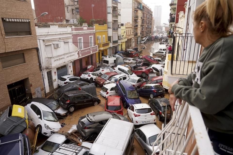 Una mujer mira por su balcón a los vehículos atrapados en la calle durante una inundación en Valencia.