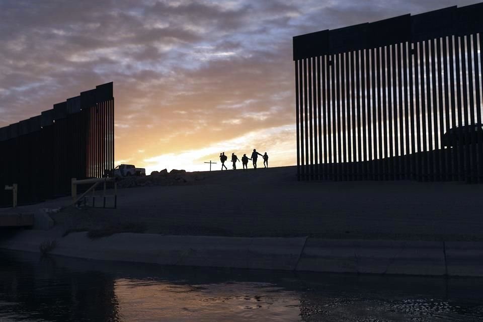 Familias migrantes cruzan por un sector del muro en la frontera, en Arizona.