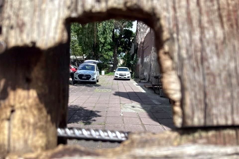 A través de un hueco entre las tablas que restringen el acceso desde la calle de Jesús María, se advierten maderas, fierros y piedra apiladas en parte del antiguo atrio y al menos tres automóviles.