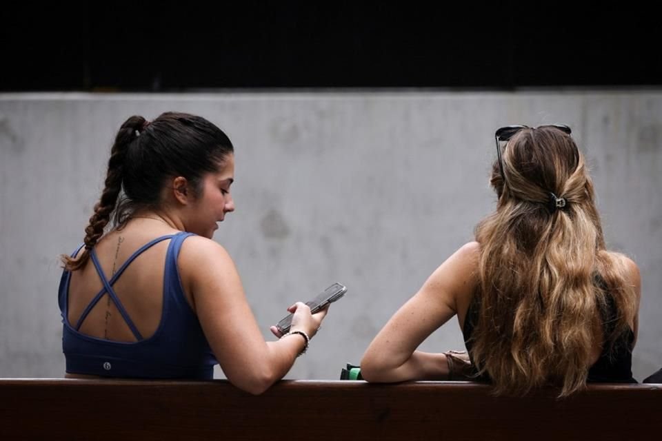 Dos mujeres se sientan en una banca con sus teléfonos en mano en Sydney, el 7 de noviembre.