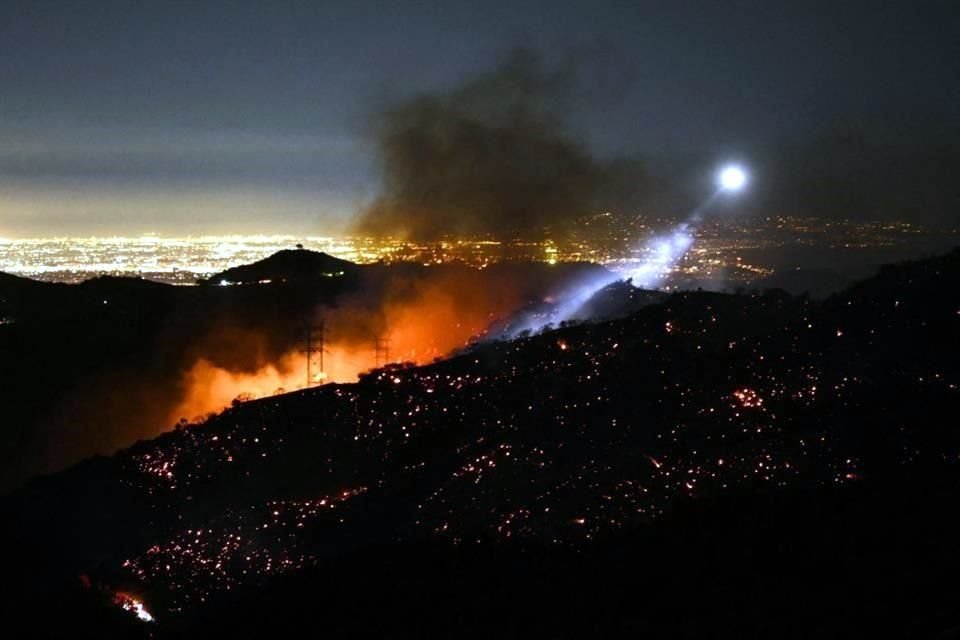 La luz de un helicóptero de extinción de incendios ilumina una ladera humeante mientras el incendio de Palisades crece cerca del vecindario de Mandeville Canyon y Encino.