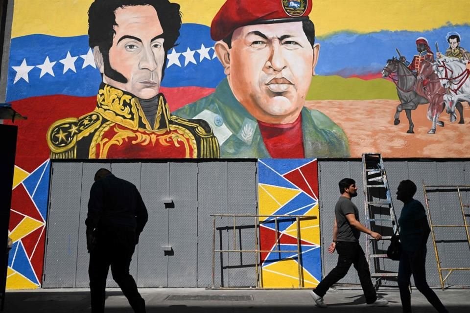 Personas caminan frente a un mural con la imagen de Hugo Chavez y Simón Bolivar, en Caracas, el 14 de enero del 2025.