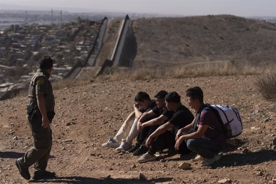 Un agente de la Patrulla Fronteriza pasa junto a cuatro hombres detenidos después de cruzar ilegalmente la frontera México-EU.