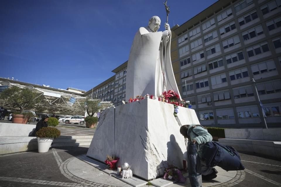 Una mujer deja una ofrenda frente a una estatua afuera del hospital donde el Papa Francisco está internado, el 16 de febrero del 2025.