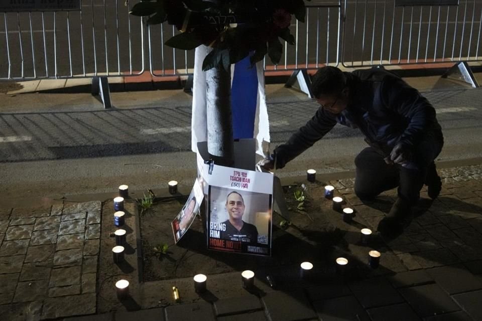 Un hombre enciende velas frente a fotografías de cuatro rehenes cuyos cadáveres fueron entregados a Israel.