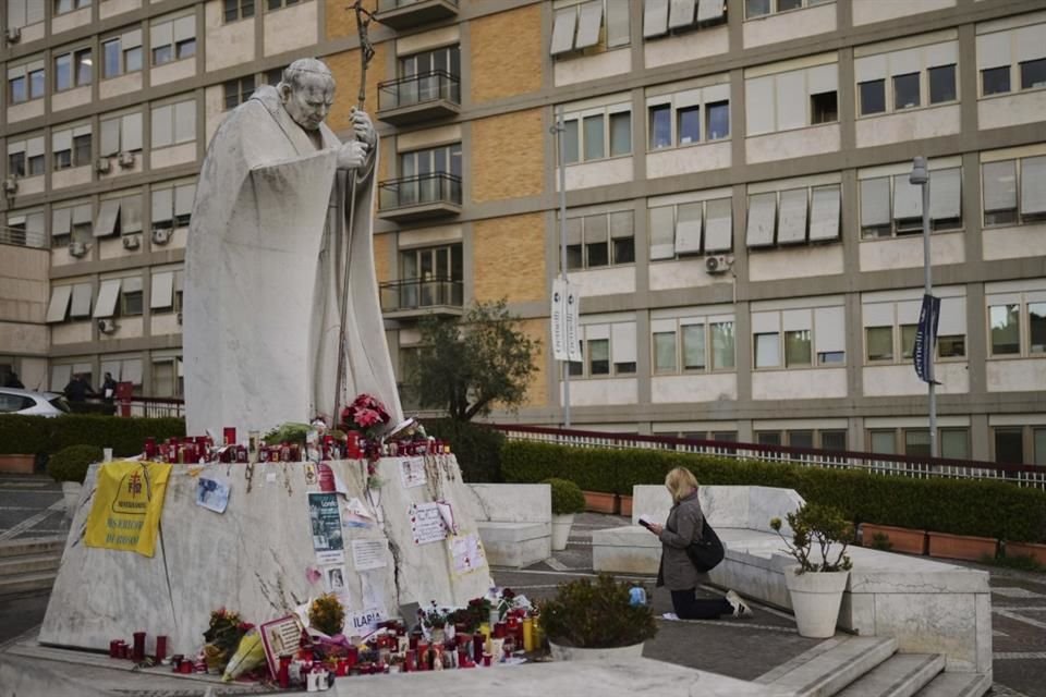 Una mujer reza junto a una estatua del Papa Juan Pablo II, a un lado del hospital donde el Papa Francisco está internado.