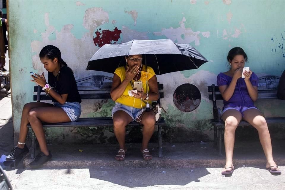 Personas en Cuba utilizan sus celulares en una banca en La Habana, en 2018.