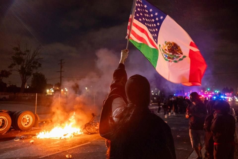 Un manifestante ondea una bandera combinada de Estados Unidos y México mientras las fuerzas del orden se enfrentan a los manifestantes durante una protesta en el vecindario de Compton en Los Ángeles.