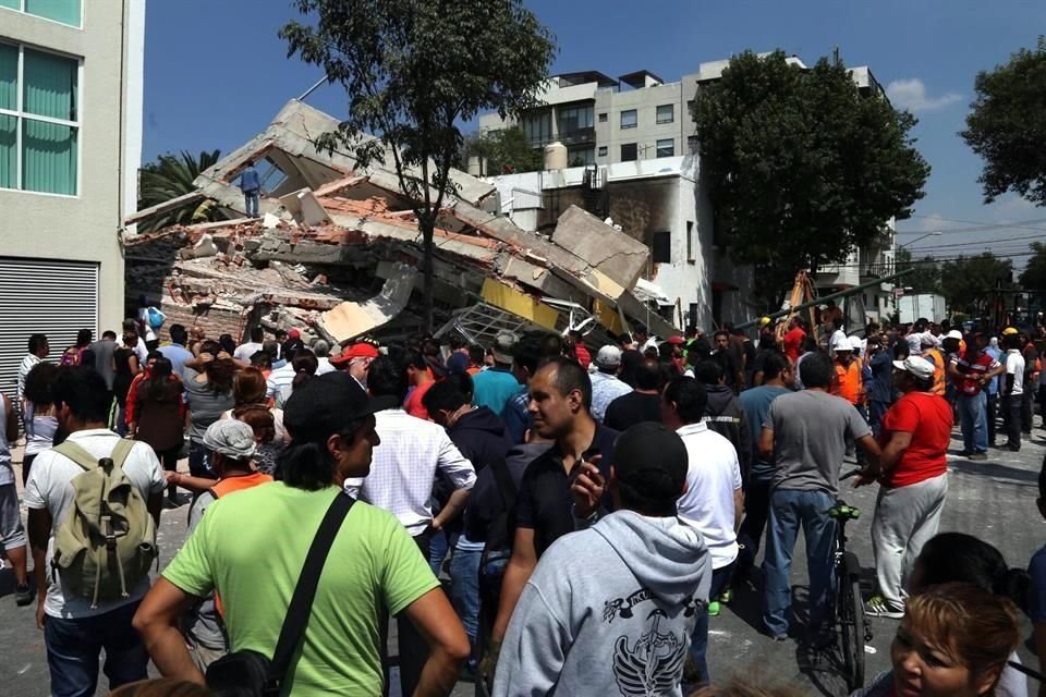 Personas caminan frente a un edificio colapsado por el temblor.
