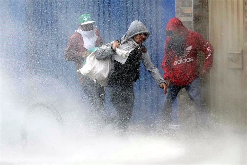 Tres personas llevan bolsas con elementos luego de ingresar a un local comercial saqueado durante las protestas este vienes, en un sector de Patio Bonito, sur de Bogotá.