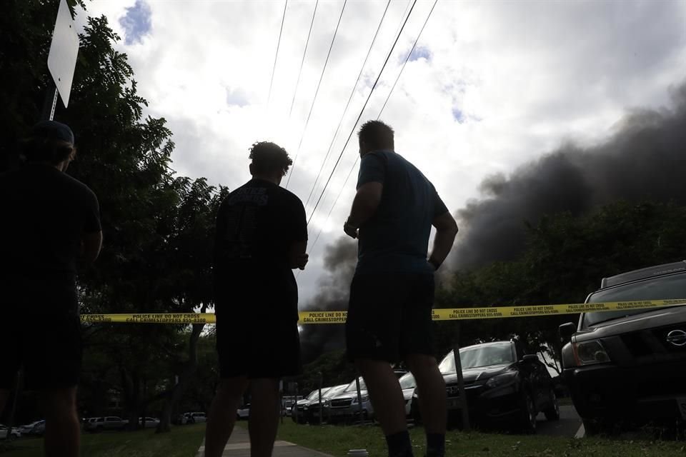 Peatones observan fuera del perímetro policial la casa en llamas del presunto agresor que mató a dos policías, en Hawái.
