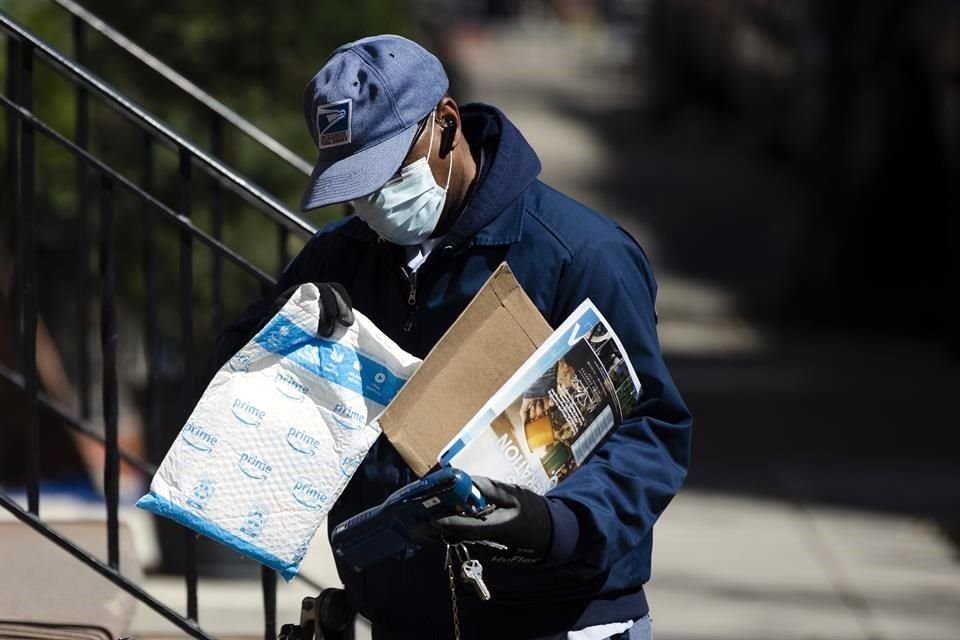 Un empleado postal en EU usa mascarilla mientras entrega el correo.