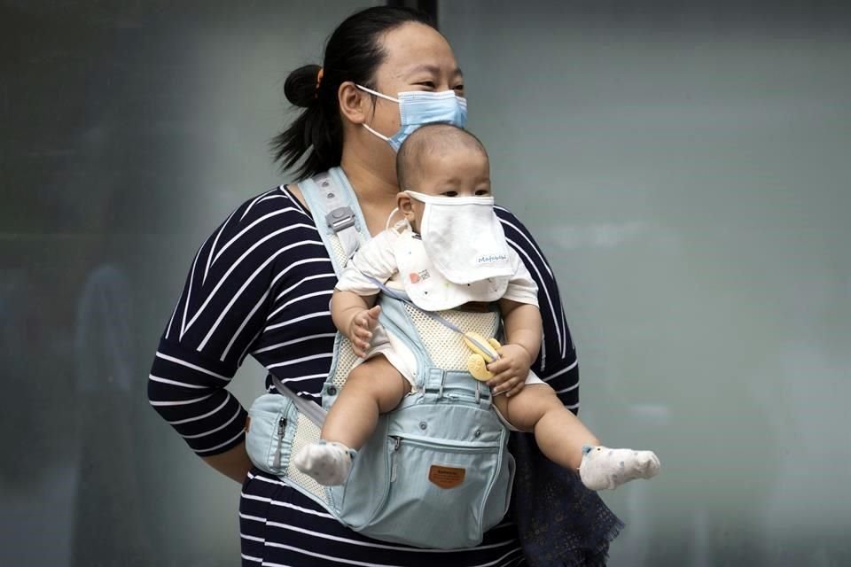 Una mujer en Beijing lleva a su bebé con el rostro cubierto.