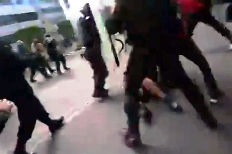 Policías rodean y patean a una manifestante en el suelo.