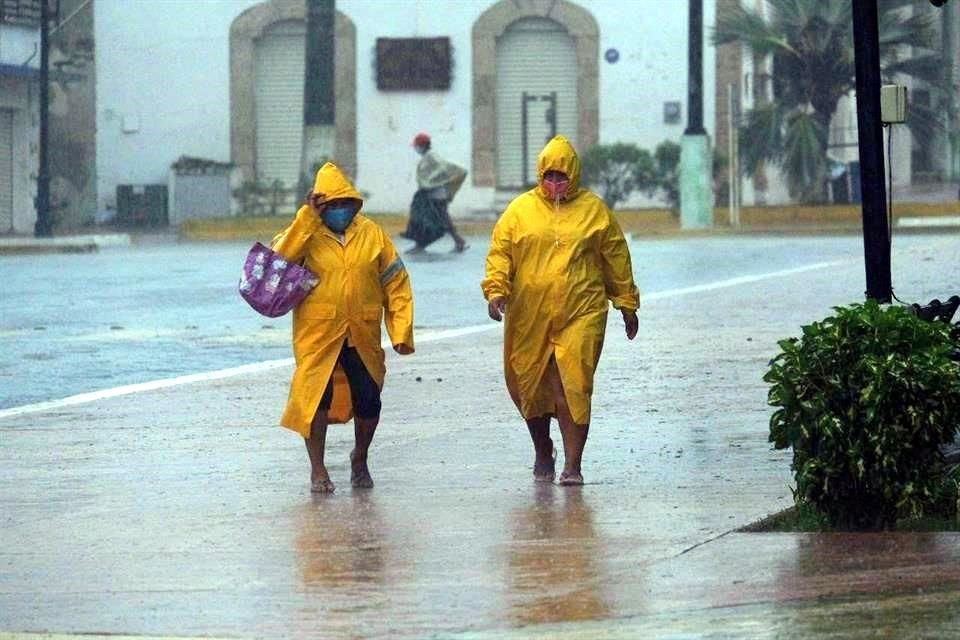 Dos personas protegidas con capas caminan en medio de un fuerte aguacero este miércoles, en Tizimín, Yucatán, donde esperan aún mas lluvias torrenciales por 'Delta'.