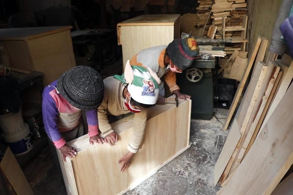 Tres de los pequeños hijos de la familia Delgado trabajan en una pieza de madera en la carpintería de su padre, en El Alto, Bolivia.