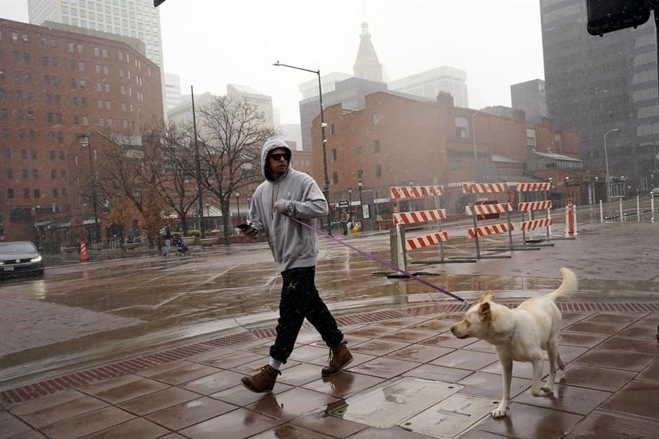Un hombre camina con su perro por las calles de Denver, mientras una tormenta que azota al centro de EU descarga lluvia en la ciudad.
