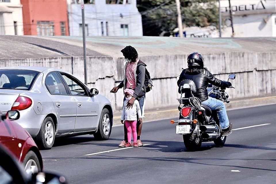 Un migrante haitiano, con su hija, pide dinero a conductores que transitan por el Viaducto Miguel Alemán, en la Ciudad de México, para seguir su camino hacia Estados Unidos.