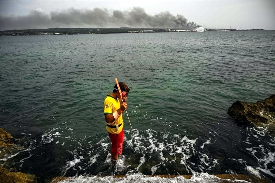 Un niño pesca en Matanzas, Cuba, con el humo del incendio de fondo, el cual es menos denso que en días anteriores.