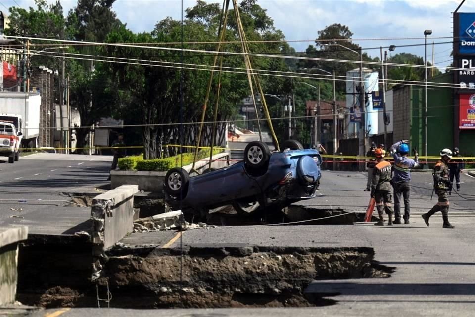 Autoridades elevan un auto que cayó en el enorme socavón que se abrió en Villa Nueva, Guatemala.