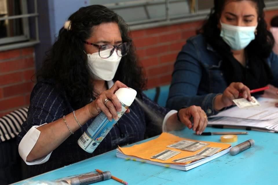 Una funcionaria de casilla en Iztapalapa rocía desinfectante a credenciales de elector.