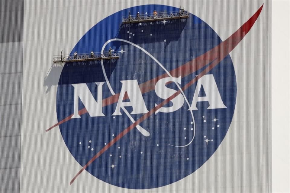 Trabajadores en andamios repintan el logotipo de la NASA en una pared del edificio de ensamblaje de vehículos espaciales en el Centro Espacial Kennedy.