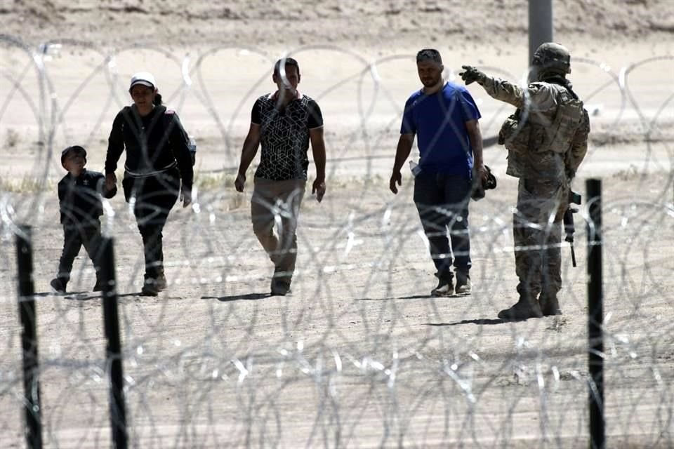 Migrantes esperan a las autoridades estadounidenses, entre una barrera de alambre de púas y la valla fronteriza en la frontera entre Estados Unidos y México.