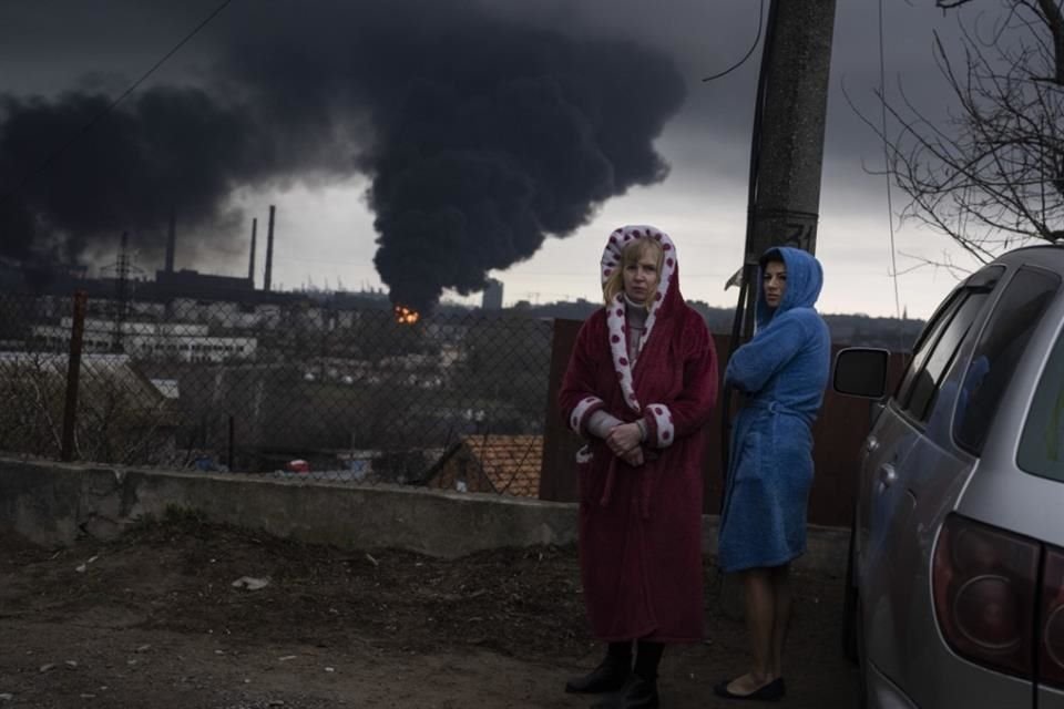 Mujeres a un lado de un auto con humo de fondo en Odesa, Ucrania, el 3 de abril del 2022.