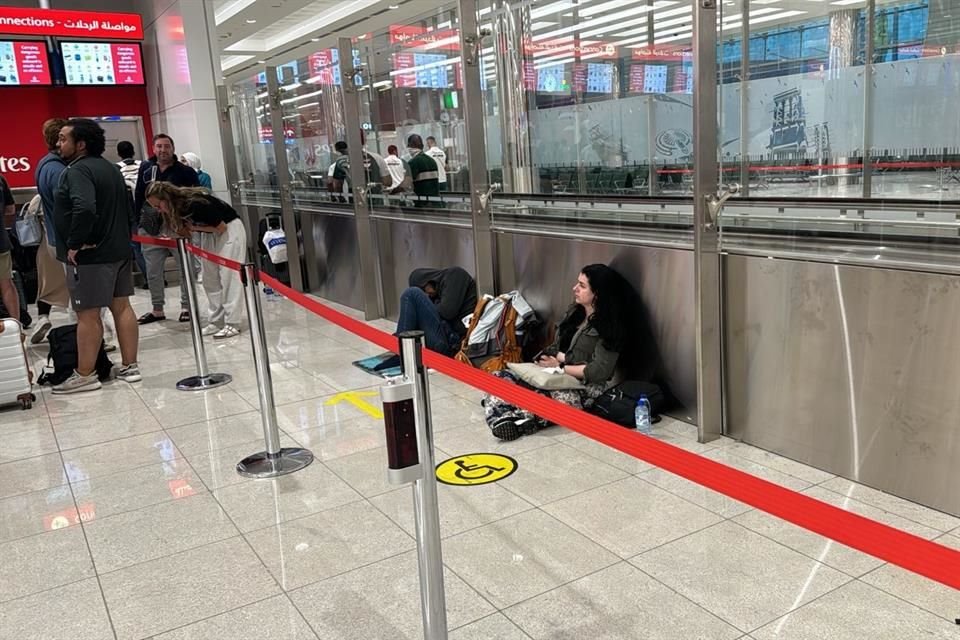 Personas esperan sentadas en el suelo una respuesta de la aerolínea Emirates tras retrasos en vuelos.