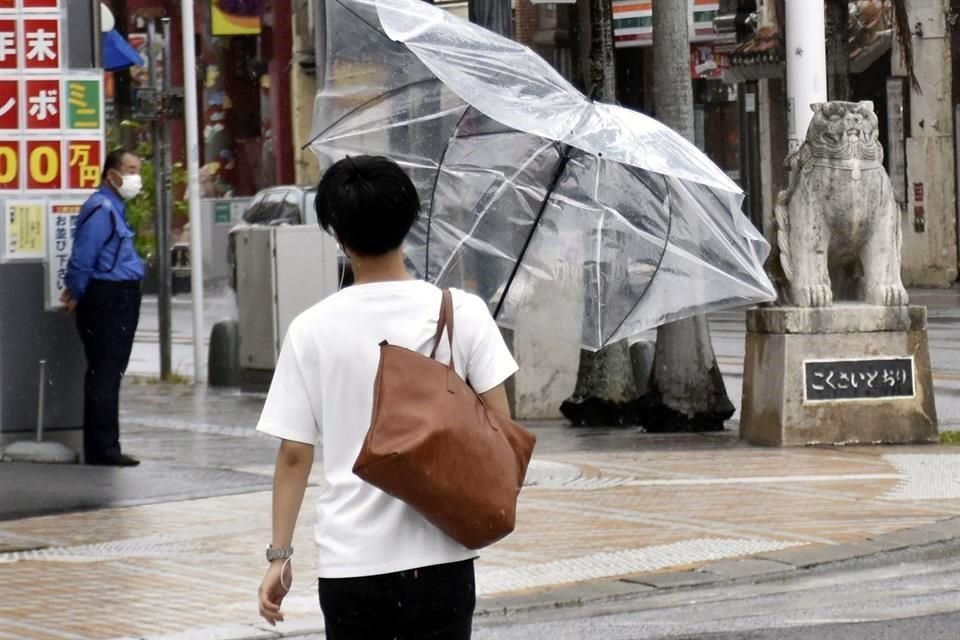 Una persona camina con un paraguas roto por la fuerza del viento en Okinawa, Japón.